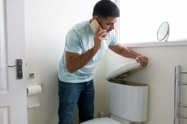 Homem no telefone abrindo o tanque do banheiro