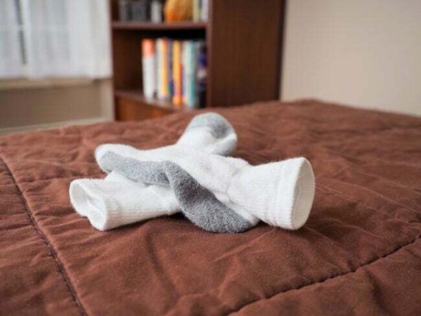 Koldt vintervejr kan kræve sokker i seng for at holde dine fødder varme, et vinterkoncept. Hvide sokker sidder oven på en brun dyne på en seng i et hjemligt soveværelse. Andre soveværelsesmøbler forbliver sløret i baggrunden, herunder en reol.