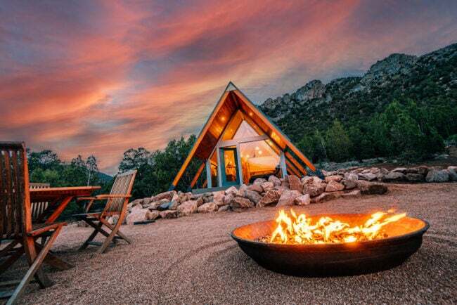 Brennende Feuerstelle auf Kiesrasen mit A-Frame-Haus und atemberaubendem Sonnenuntergang im Hintergrund
