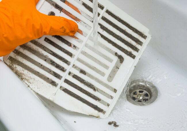 Mão enluvada limpando um filtro de ventilador de banheiro empoeirado na pia