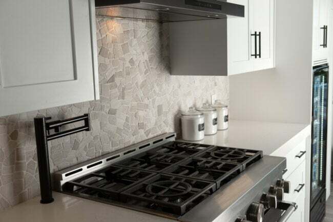 Moderní kuchyně se světle šedým dlaždicovým pozadím a nerezovým plynovým sporákem