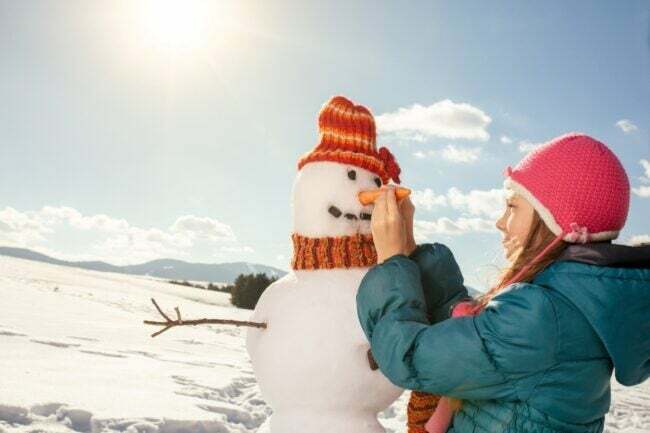 Una niña agregando una nariz de zanahoria a un muñeco de nieve