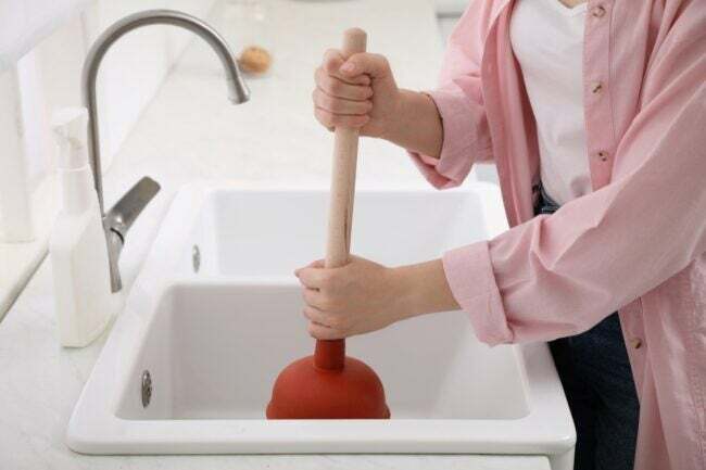 Az a személy, aki dugattyút használ a mosogató eltömődésének feloldására