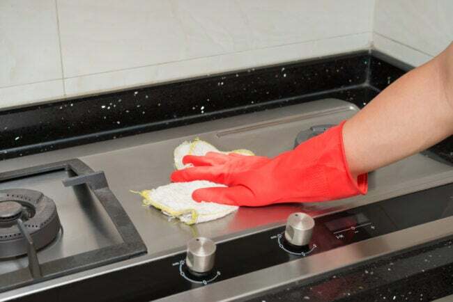 кокосова олія використовує витирання плити з нержавіючої сталі ганчіркою в червоних рукавичках 