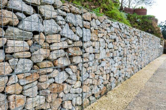 Жичана габионска камена ограда. Метални кавез испуњен камењем. Текстура позадине камене ограде са кавезом.