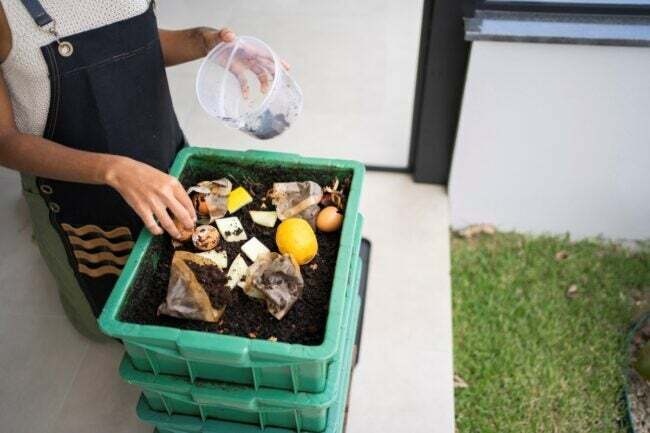 Kvinne legger kjøkkenrester i grønn kompostbeholder