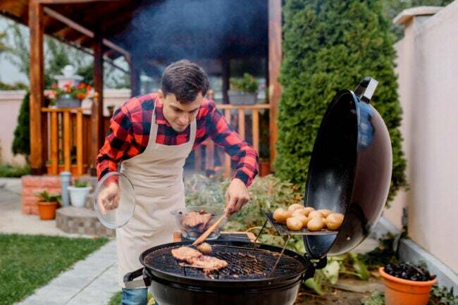 kuinka hävittää esiliinassa oleva grillimies, joka paistaa lihaa pyöreällä grillillä takapihalla