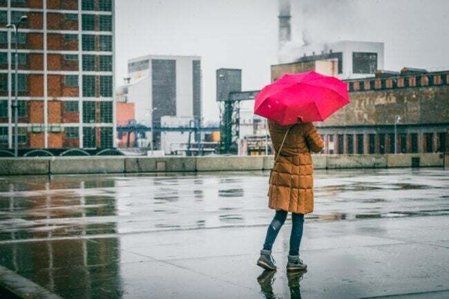 kvinde med rød paraply stående udenfor i regnen