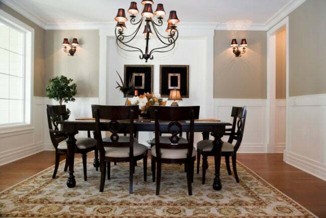 전통적인 스타일의 검은색 식탁과 의자, 검은색 샹들리에 아래, 흰색 웨인스코팅이 있는 베이지색 방
