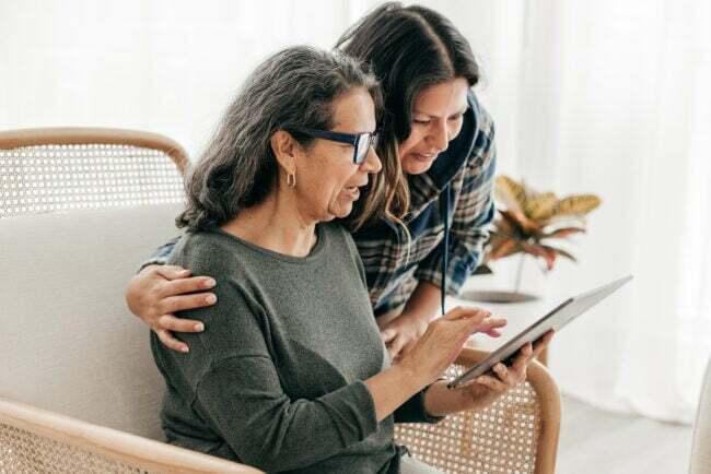mujer ayudando a una mujer mayor a usar un sistema doméstico inteligente en un dispositivo de tableta
