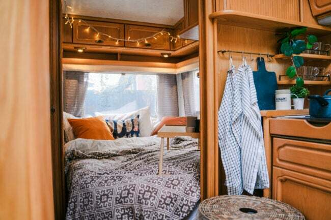 иСтоцк-1413621524 Декоративни кревет за кампер у малом камперу са лепим прекривачем и јастуцима