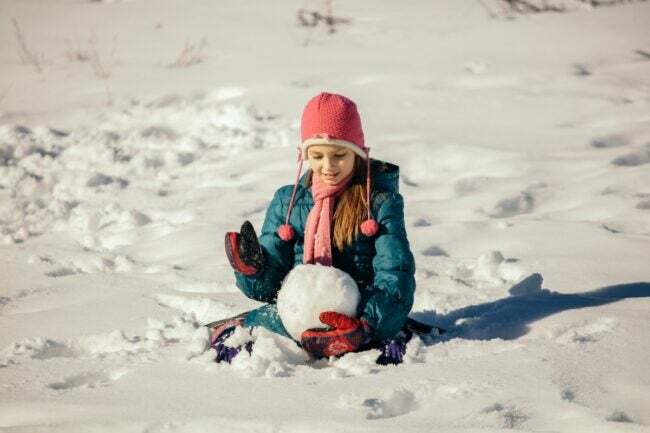Chica formando la cabeza de un muñeco de nieve en la nieve.