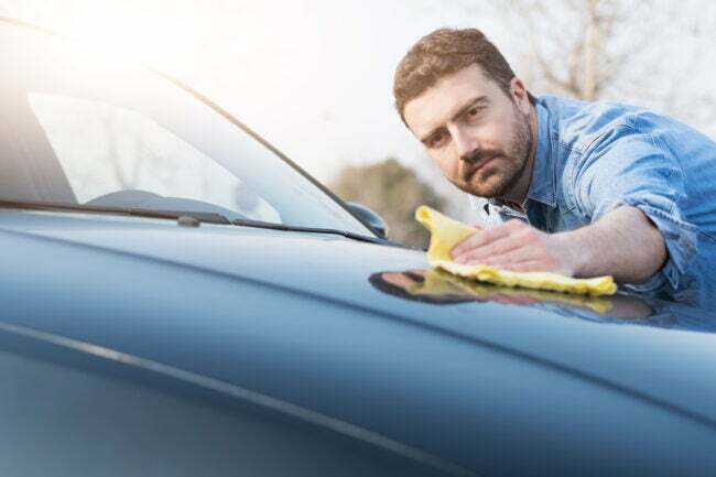 Mies käyttää liinaa auton konepellin puhdistamiseen