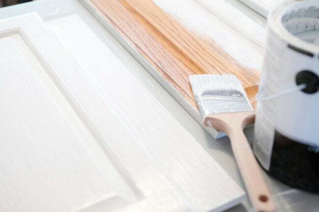 Weiße Farbe mit niedrigem VOC-Gehalt auf Holzschränken mit nassem Pinsel und Farbdose