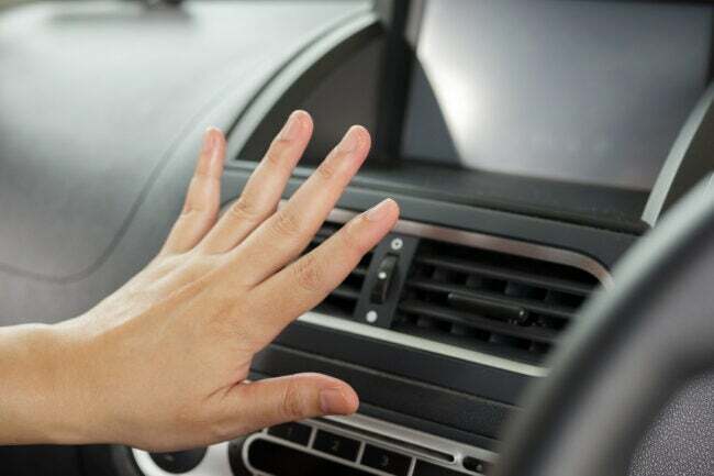 personne sentant la température du climatiseur de voiture avec la main devant les bouches d'aération