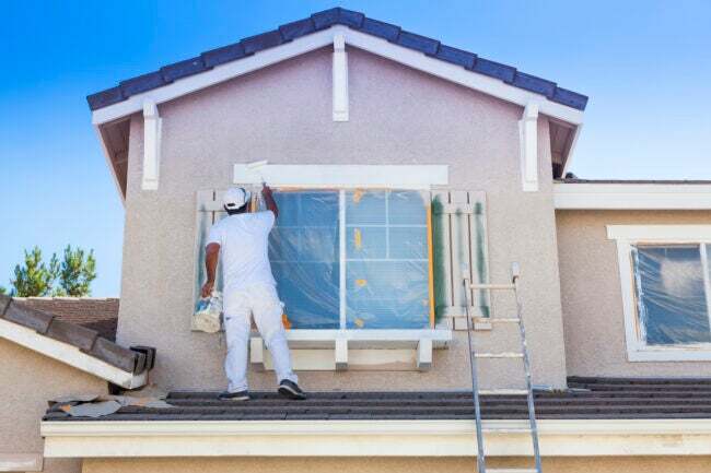 Zaneprázdněný malíř domů maluje čalounění a okenice domu.