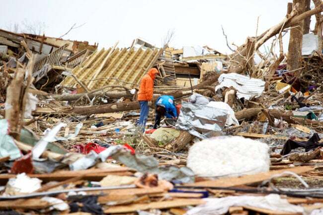 dos hombres mirando a través de los escombros después de un tornado.