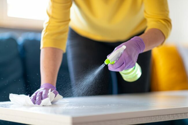 Mulher limpando mesa com spray usando luvas descartáveis ​​roxas