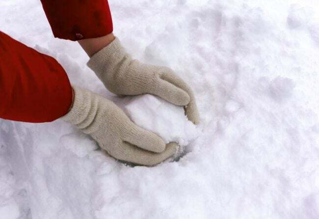 Pirštinuotos rankos formuoja sniego gniūžtę