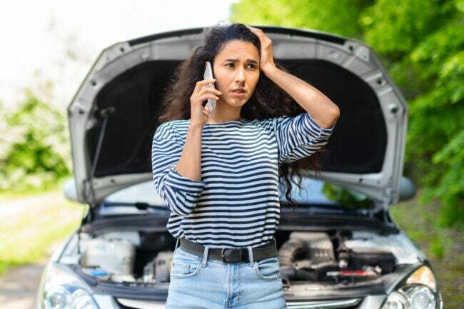 Нервна жена с отворен капак на кола се обажда на автосервиз