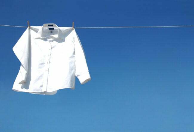 eine frische weiße Bluse, die vor strahlend blauem Himmel an der Wäscheleine hängt