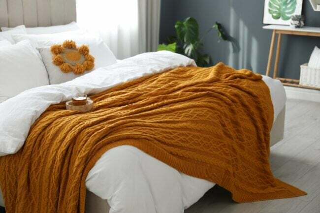 रोएंदार सफेद चादर और नारंगी बुनाई के साथ आरामदायक बिस्तर।