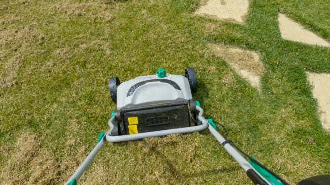  裏庭の芝生の世話をしながら、グラスエアレーターを使用する庭師。 緑の芝生の成長を促進するための春の家庭菜園作業の一人称視点。 造園用の実用機械です。