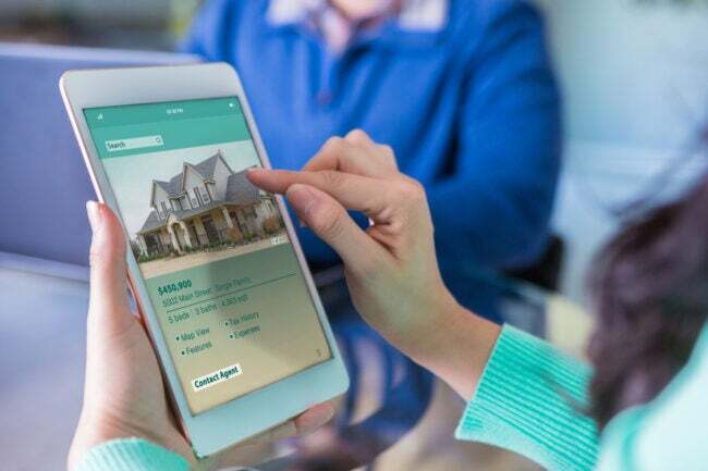 Detalhe do tablet sendo usado para comprar uma casa com a imagem de uma casa grande com preço listado