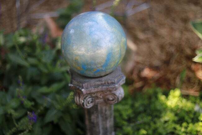 Серебряный-металлический-сад-шар-глядящий-сидит на-столбе-подставке-в-саду.