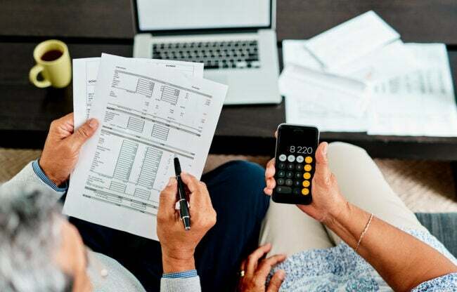 foto aérea de pessoas olhando para documentos financeiros e uma segurando uma calculadora de iphone