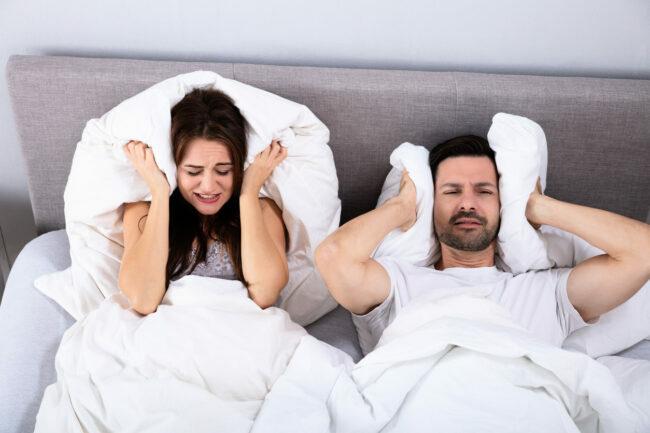 Uznemireni par koji pokriva uši jastukom na krevetu