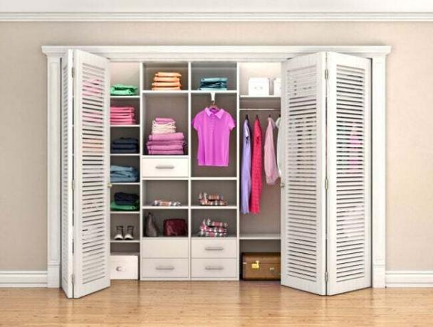 خزانة ذات أبواب بيضاء ثنائية الطي ذات فتحات تهوية أمامية للخزانة مع ملابس مشرقة