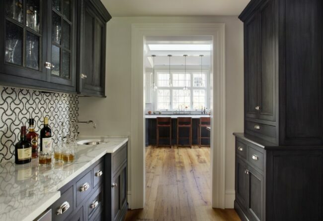 Butlerova komora s čiernymi skrinkami a mramorovými pultmi; pohľad do kuchyne cez dvere