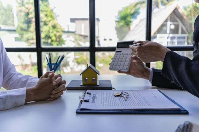 homem segurando a calculadora para mostrar a outra pessoa com a casa na mesa ilustrando o conceito imobiliário