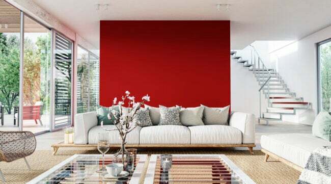 Eine leuchtend rote Akzentwand bildet den Hintergrund für ein luftiges Wohnzimmer mit weiß-braunem Dekor