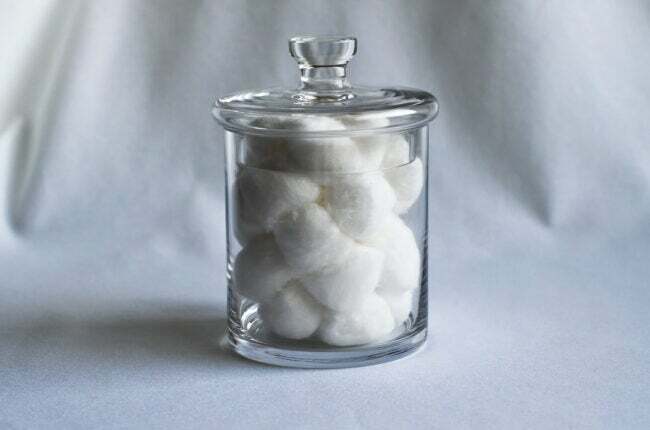 Bolas de algodão em frasco de vidro em um lençol branco.