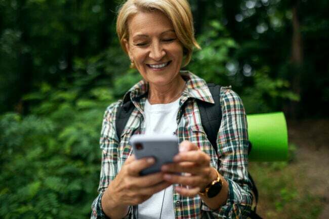 Alpinista feminina madura sorrindo enquanto olha para o telefone em uma trilha