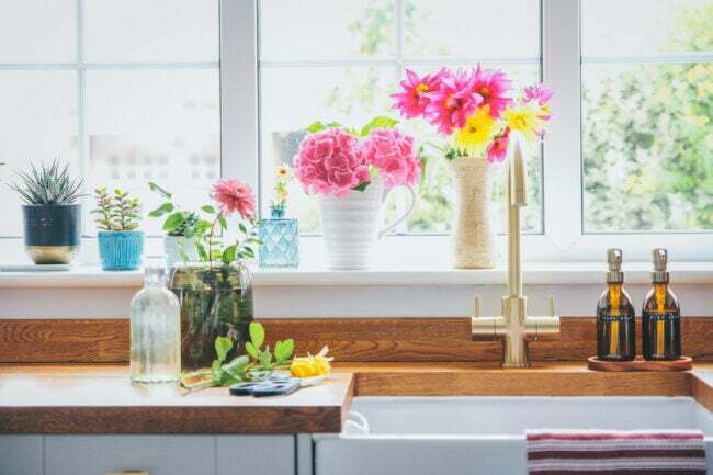მოჭრილი ყვავილების ბაღის თაიგულები მზიანი სამზარეულოს ფანჯრის რაფაზე