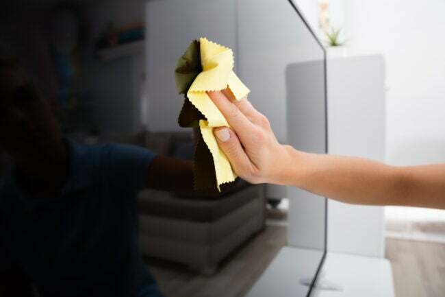 Iš arti vaizdas, kai televizoriaus ekranas valomas rankomis mikropluošto šluoste