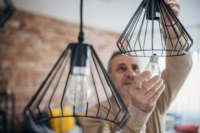 Um homem troca sozinho uma lâmpada em um apartamento