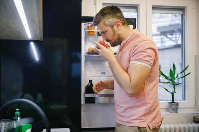 Homem cheirando tomate na geladeira
