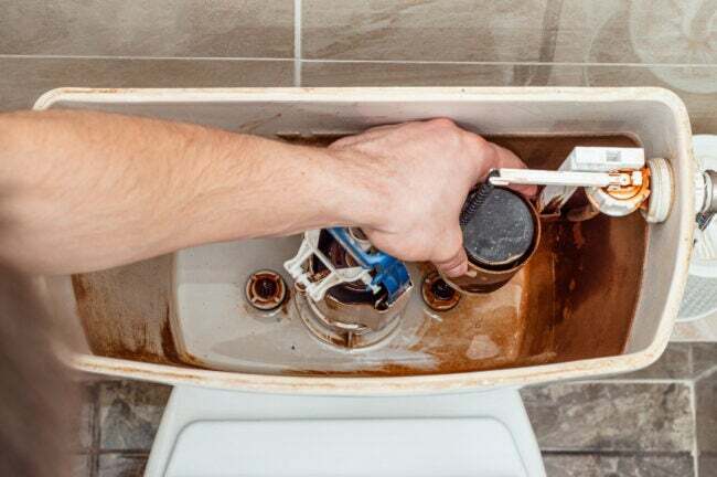 Mão removendo a válvula de enchimento do vaso sanitário do tanque
