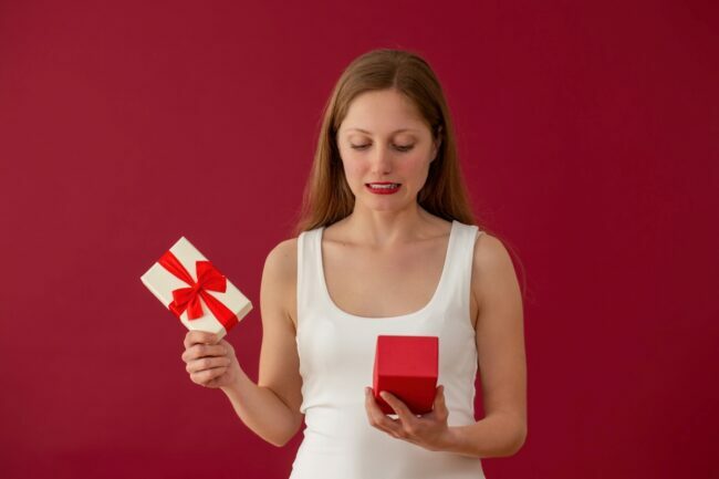 Mujer abriendo regalo con mirada avergonzada en su rostro