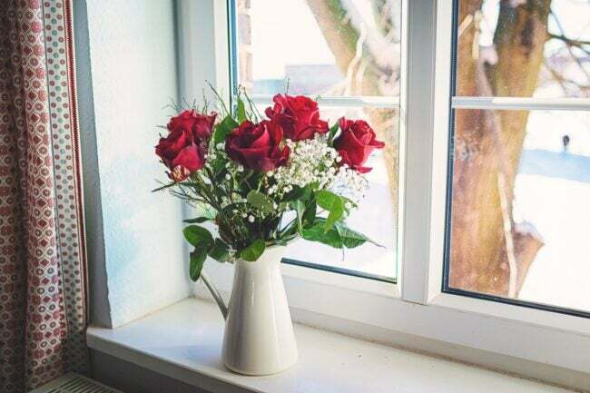 Vörös rózsák vázában az ablakpárkányon