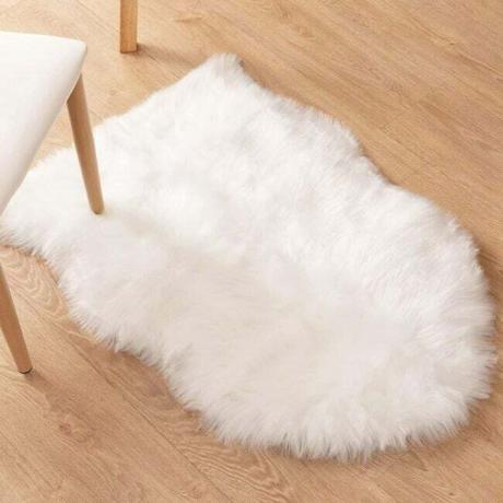 Biały dywanik z owczej skóry ze sztucznego futra na jasnej drewnianej podłodze