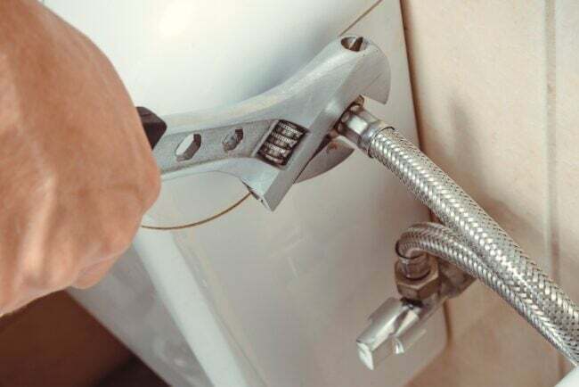 Tangan menggunakan kunci pas yang dapat disesuaikan untuk mematikan suplai air toilet