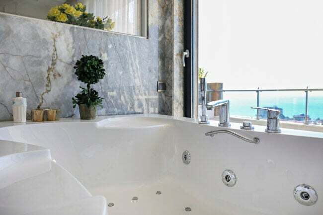 гидромассажная ванна в углу ванной комнаты у окна с мраморной стеной