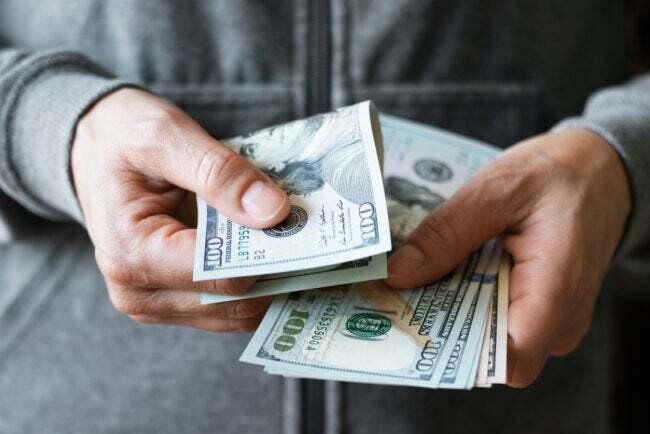 muž v šedé mikině drží peníze v rukou