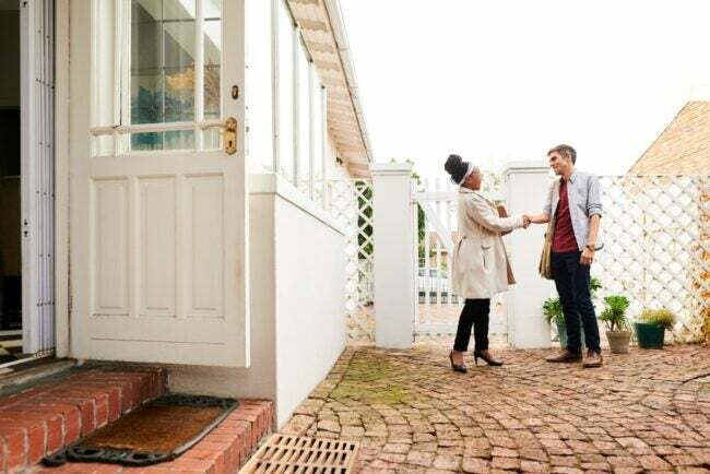 Жена се рукује са мушкарцем испред куће
