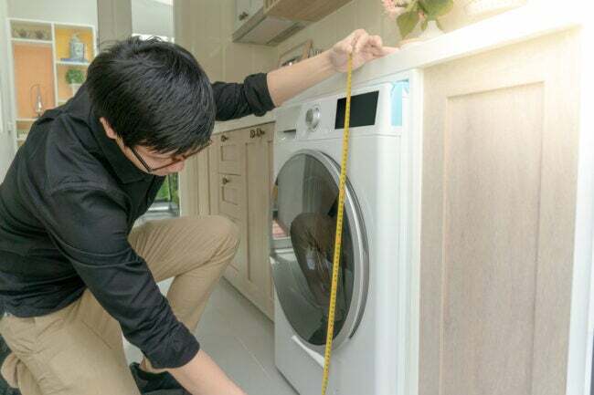 iStock-1035884128 Home Depot homem de compras medindo a altura da máquina de lavar